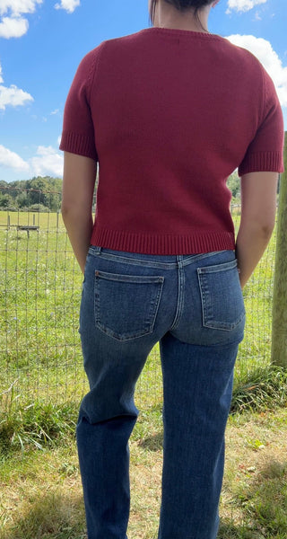 Back view of a cherry red short-sleeve knit cardigan paired with high-rise dark wash denim jeans.