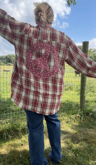 Back view of a red plaid flannel shirt featuring a large burgundy floral peace sign patch, styled with classic blue jeans.