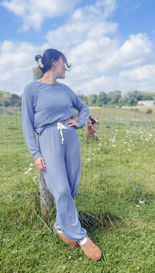 Woman in blue and white striped lounge set with drawstring waist standing in a sunny pasture, casual boutique fall style.