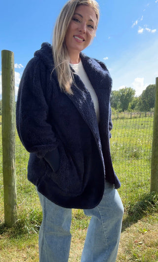 Navy blue faux-fur hooded coat with cozy texture, paired with light-wash wide-leg jeans for a chic cold-weather look.