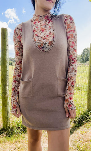 Close-up of taupe knit jumper dress with deep V-neck layered over a floral long-sleeve mock-neck top for fall styling.