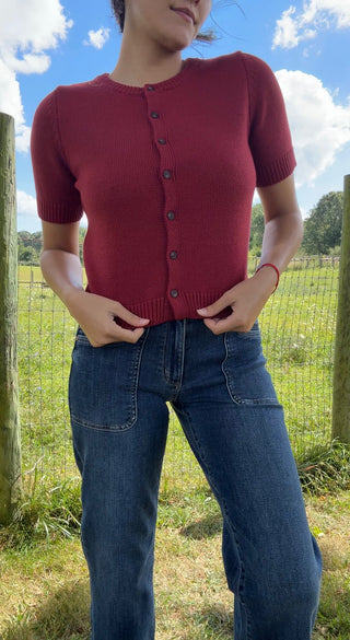 Close-up of a cherry red short-sleeve button-up cardigan styled with high-rise dark wash denim jeans.