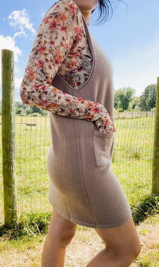 Side view of taupe knit jumper dress with front pocket, layered over a floral mock-neck top for chic fall style.