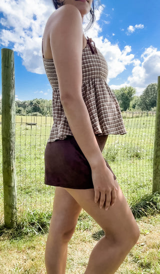 Side view of woman in brown gingham peplum tank with bow straps and brown mini skirt, chic fall boutique outfit.