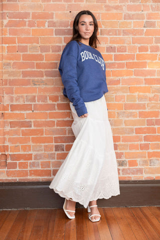 White tiered maxi skirt with delicate eyelet embroidery and a drawstring waist, styled with minimalist white sandals for a breezy look.