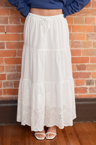 White tiered maxi skirt with delicate eyelet embroidery and a drawstring waist, styled with minimalist white sandals for a breezy look.