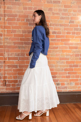 White tiered maxi skirt with delicate eyelet embroidery and a drawstring waist, styled with minimalist white sandals for a breezy look.