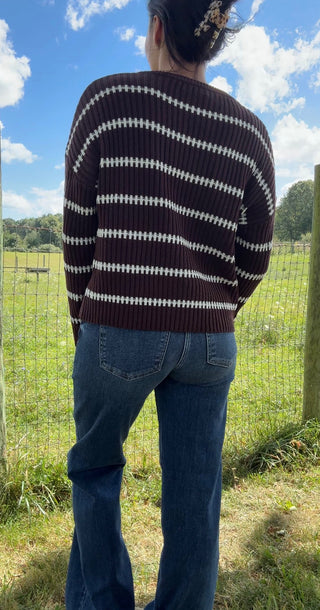 Back view of brown ribbed sweater with white diagonal stripes paired with high-waisted blue jeans outdoors.