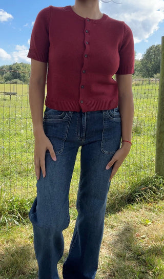 Front view of a fitted cherry red short-sleeve button-up cardigan paired with high-rise dark wash jeans.