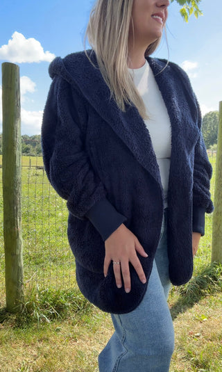 “Woman in a cozy navy blue sherpa coat with pockets over a white tee and light wash jeans outdoors.”