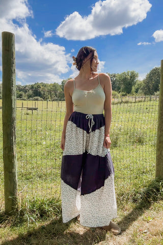 Woman in a cream camisole and tiered wide-leg pants featuring navy and white floral panels with a drawstring waist.