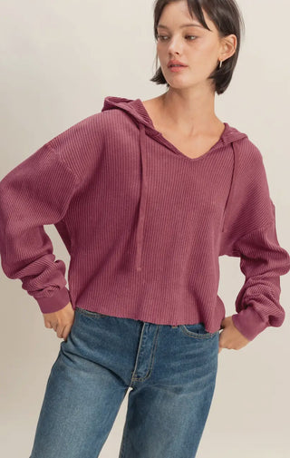 Woman in a cropped berry waffle-knit hoodie with drawstrings, paired with high-rise blue jeans.
