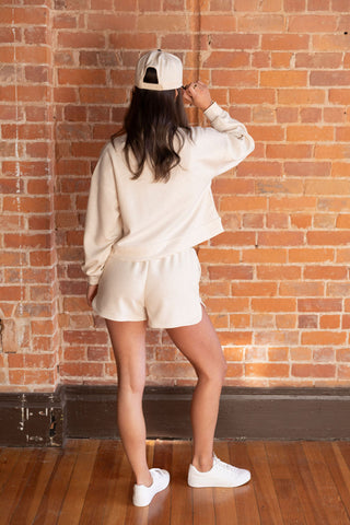 Casual chic in a cream half-zip pullover and matching high-waisted shorts, paired with white sneakers and a baseball cap