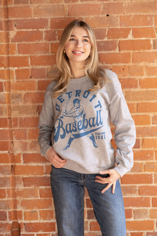Retro-inspired Detroit baseball sweatshirt in gray with blue graphic print, styled with relaxed-fit jeans.