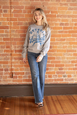 Retro-inspired Detroit baseball sweatshirt in gray with blue graphic print, styled with relaxed-fit jeans.