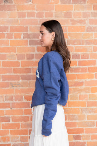 Oversized blue sweatshirt with 'Book Club' print, tucked into a breezy white tiered skirt with lace-like embroidery details.