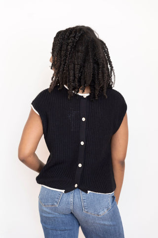 Back view of black knit button-up sweater with contrast white trim, styled with blue denim jeans for a casual-chic look.