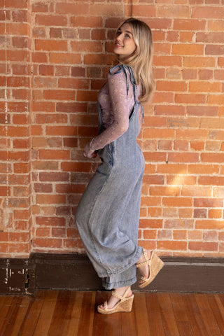 Light-wash denim overalls with wide legs, paired with a sheer floral blouse. Effortless boho-chic fashion statement.