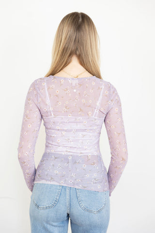 Woman wearing a sheer lilac floral long-sleeve top with delicate embroidery, layered over a matching tank, styled with light-wash jeans.