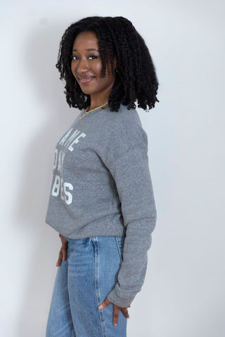 A woman in a cozy gray sweatshirt with "Game Day Vibes" text, styled with relaxed-fit denim, posing with a confident smile