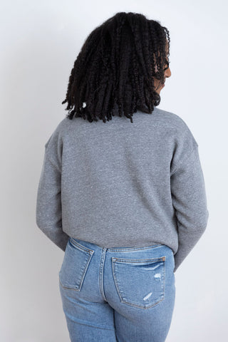 A  woman in a heather gray crewneck sweatshirt showing back view, paired with classic blue jeans.