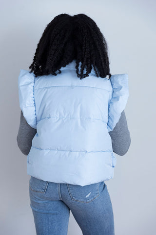 Stylish light blue puffer vest with feminine ruffle accents, perfect for layering over casual outfits for a cozy yet fashionable vibe.