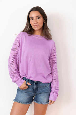 Lilac knit sweater with crochet-style sleeves, paired with denim cutoffs. A trendy spring-to-summer pullover with a relaxed fit.