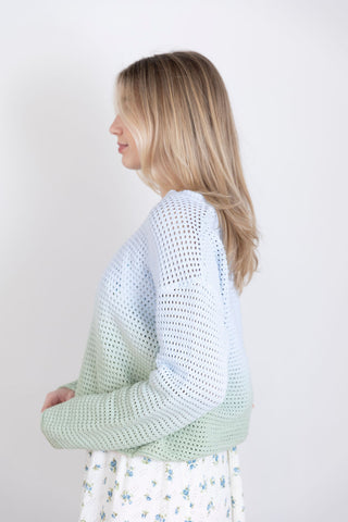 Model wearing a pastel ombre crochet sweater in blue and green, paired with a floral midi skirt. Lightweight, breathable knit for spring styling.